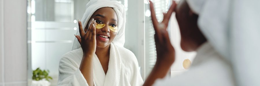 A person wearing a bathrobe looking in a bathroom mirror while applying skin-care product.
