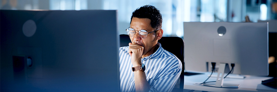 A tired person sitting in front of a computer and yawning.