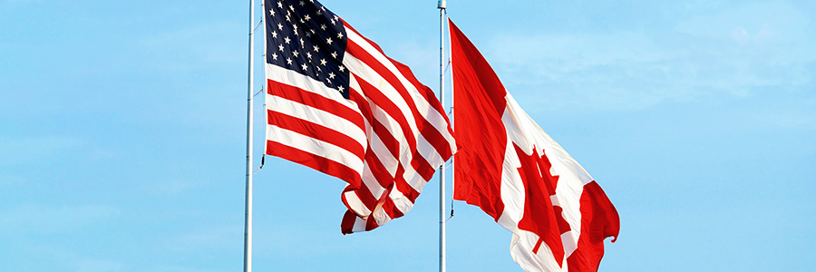 The American and Canadian flags flying together against a blue sky.