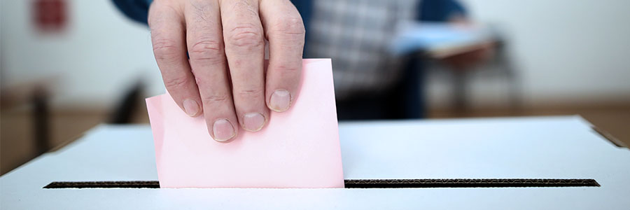 Close up of a hand inserting a piece of paper into an election ballot box.