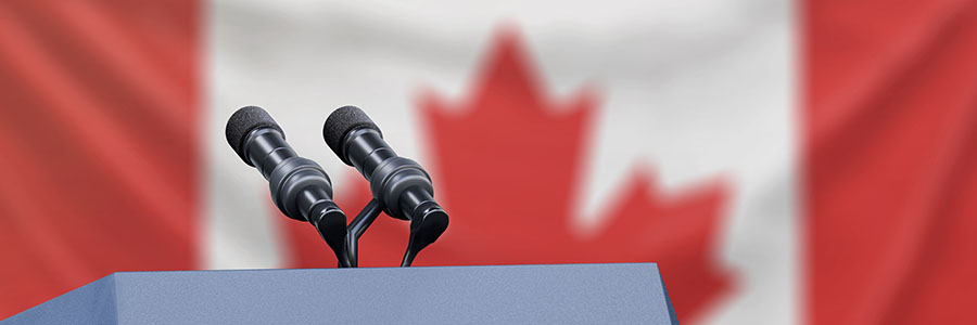 A speakers pedestal with two microphones with a Canadian flag in the background.