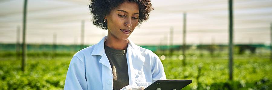 A woman in a greenhouse looking at a tablet computer.