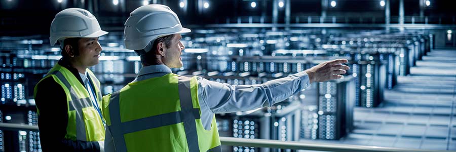 Construction workers in high-visibility vests discussing and looking over a data center floor filled with server racks.