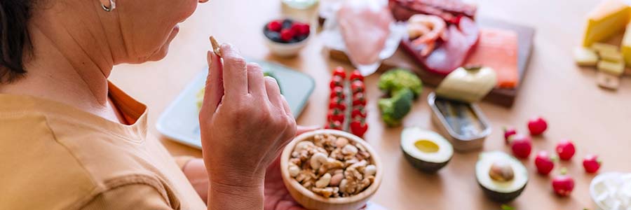A person eating nuts, surrounded by healthy, fresh food on a table.